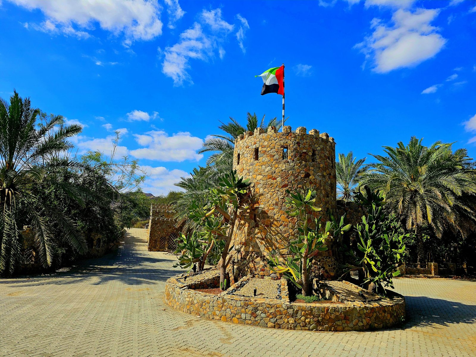 A stone tower with a flag, framed by palm trees, showcasing the scenic view Mughaibar Fort Resort in Hatta.