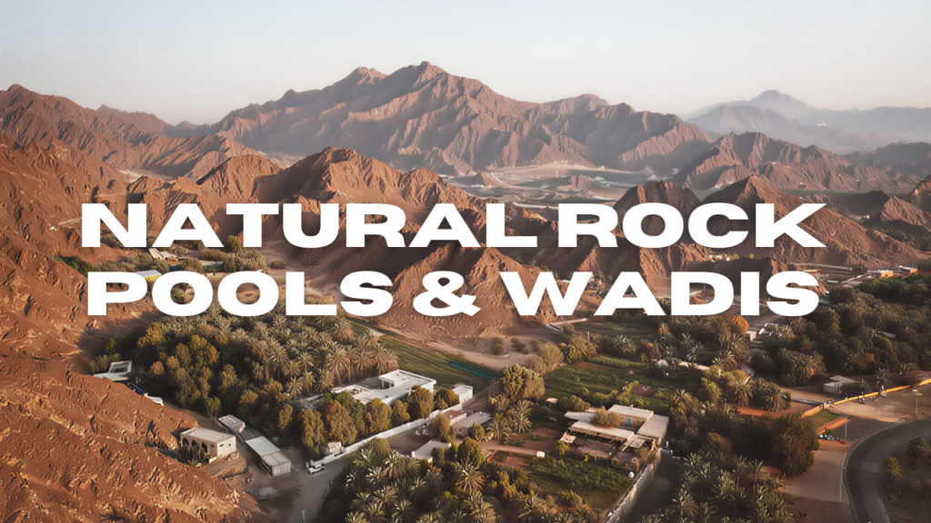 Aerial view of Hatta's natural rock pools and wadis (dry riverbeds) surrounded by palm trees and mountains.